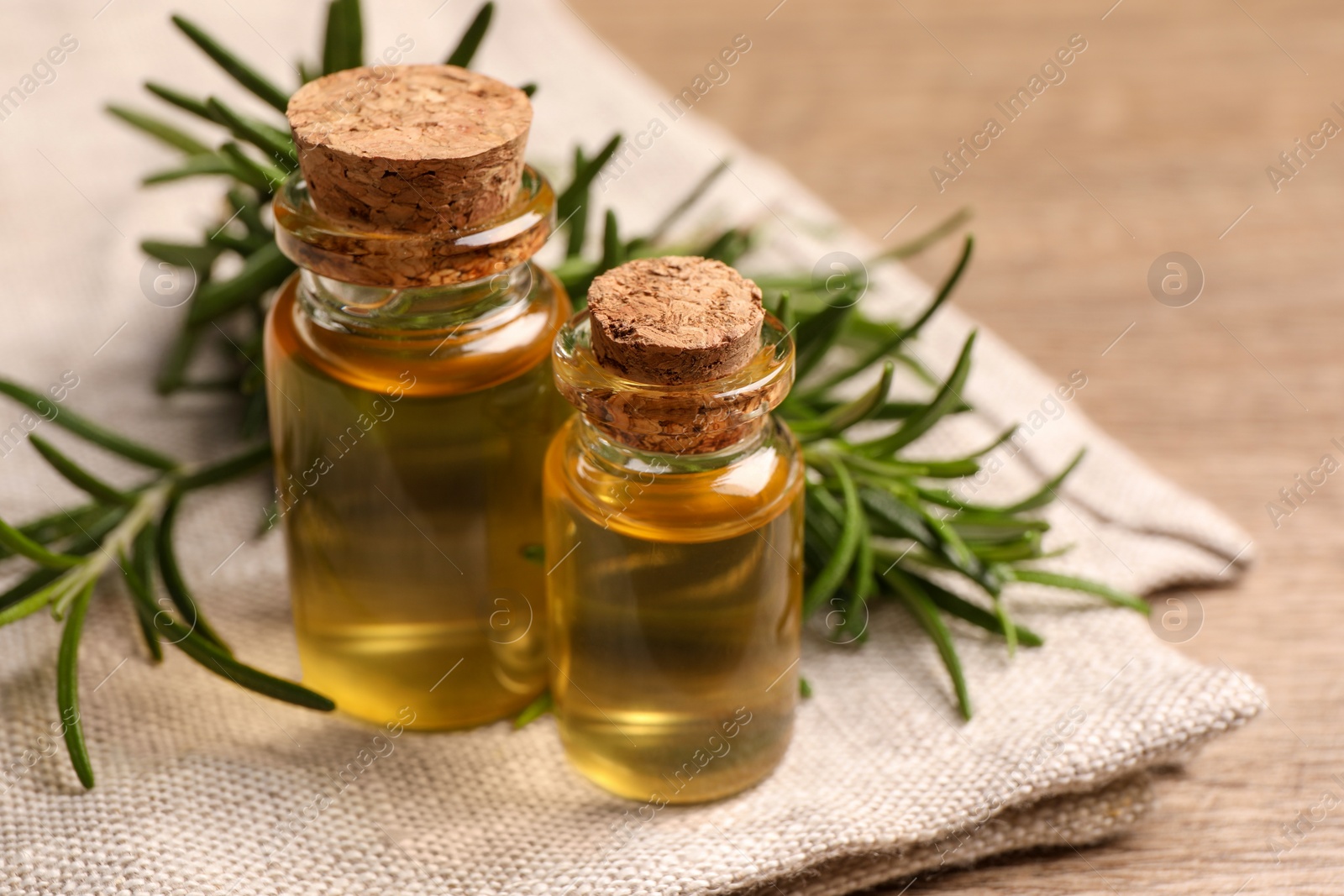 Photo of Bottles with essential oil and fresh rosemary on wooden table, closeup