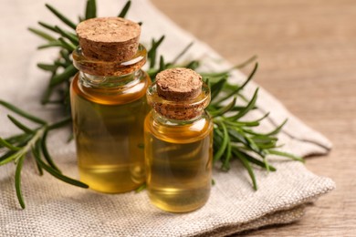 Bottles with essential oil and fresh rosemary on wooden table, closeup