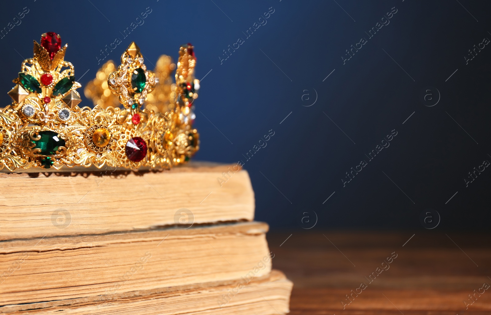 Photo of Beautiful golden crown on old books against dark blue background, space for text. Fantasy item