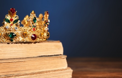 Photo of Beautiful golden crown on old books against dark blue background, space for text. Fantasy item