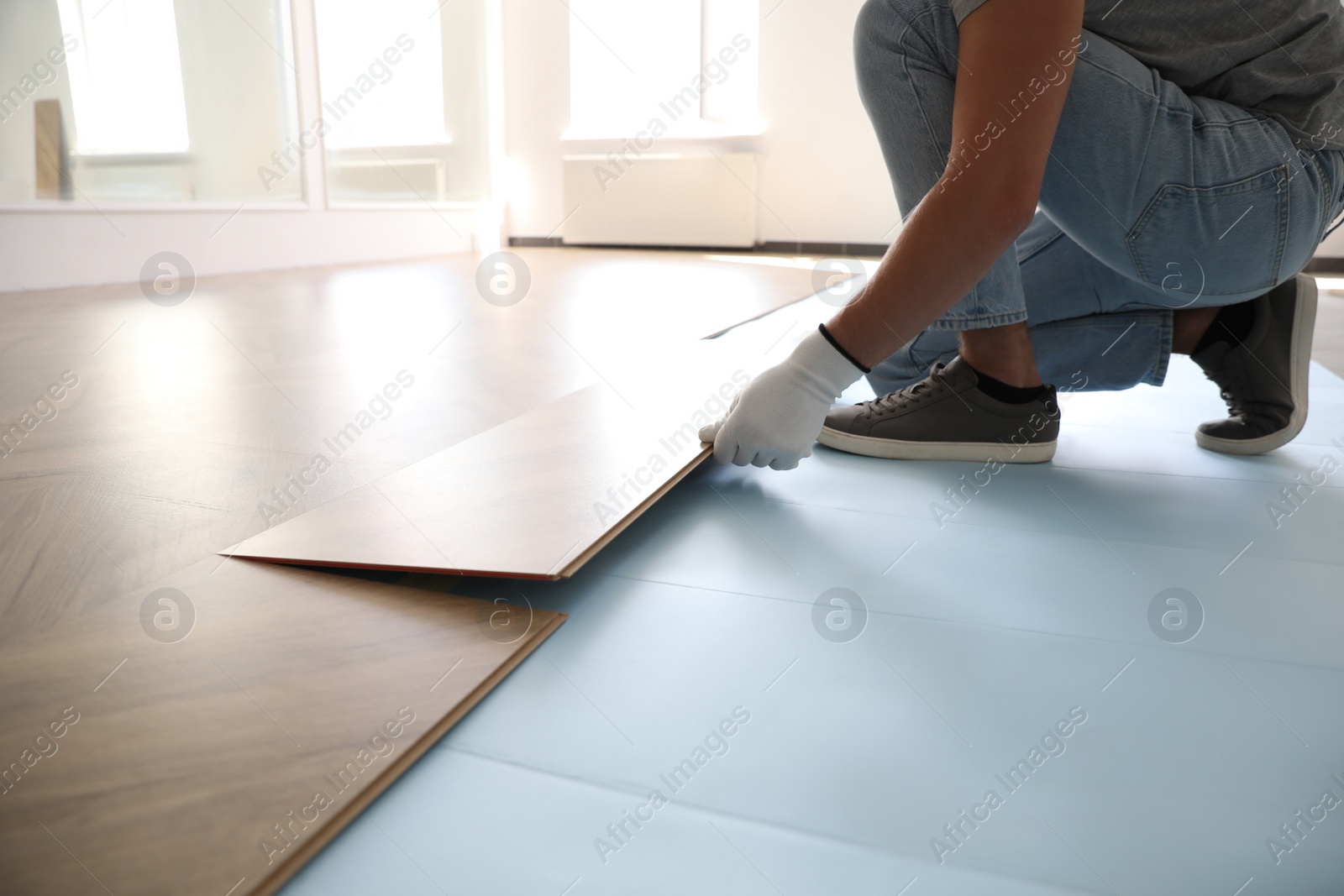 Photo of Worker installing laminated wooden floor indoors, closeup