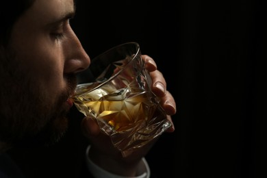 Man drinking whiskey on black background, closeup. Space for text