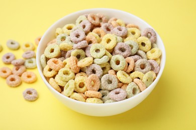 Photo of Tasty cereal rings in bowl on yellow table, closeup