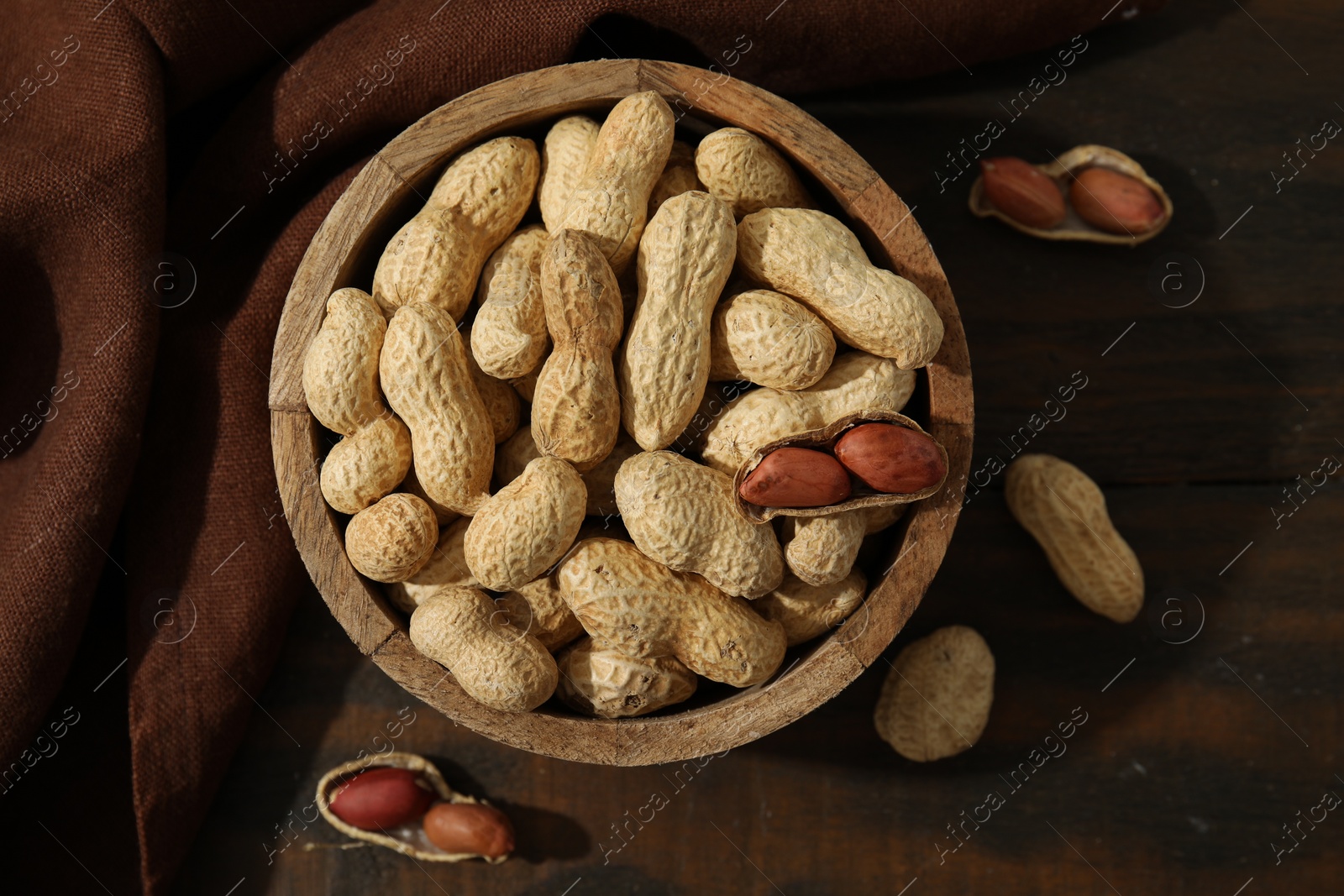 Photo of Fresh unpeeled peanuts in bowl on wooden table, top view