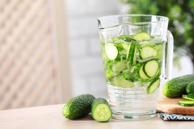 Photo of Refreshing cucumber water in jug and vegetables on light wooden table, closeup. Space for text