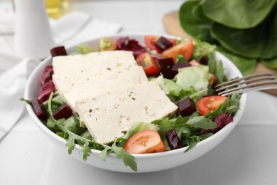 Photo of Bowl of tasty salad with tofu and vegetables on white tiled table, closeup