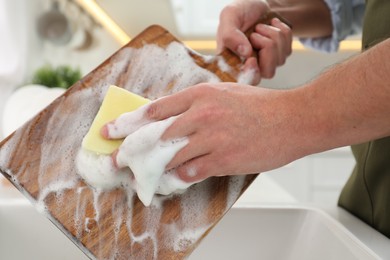Photo of Man washing wooden cutting board in kitchen, closeup