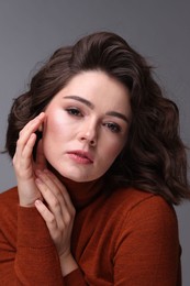 Portrait of beautiful young woman with wavy hairstyle on grey background