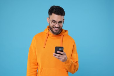 Photo of Happy young man using smartphone on light blue background