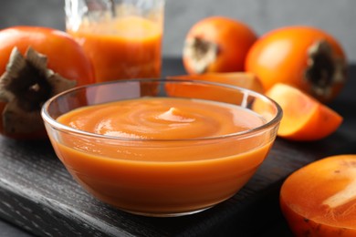 Delicious persimmon jam in glass bowl and fresh fruits on table, closeup