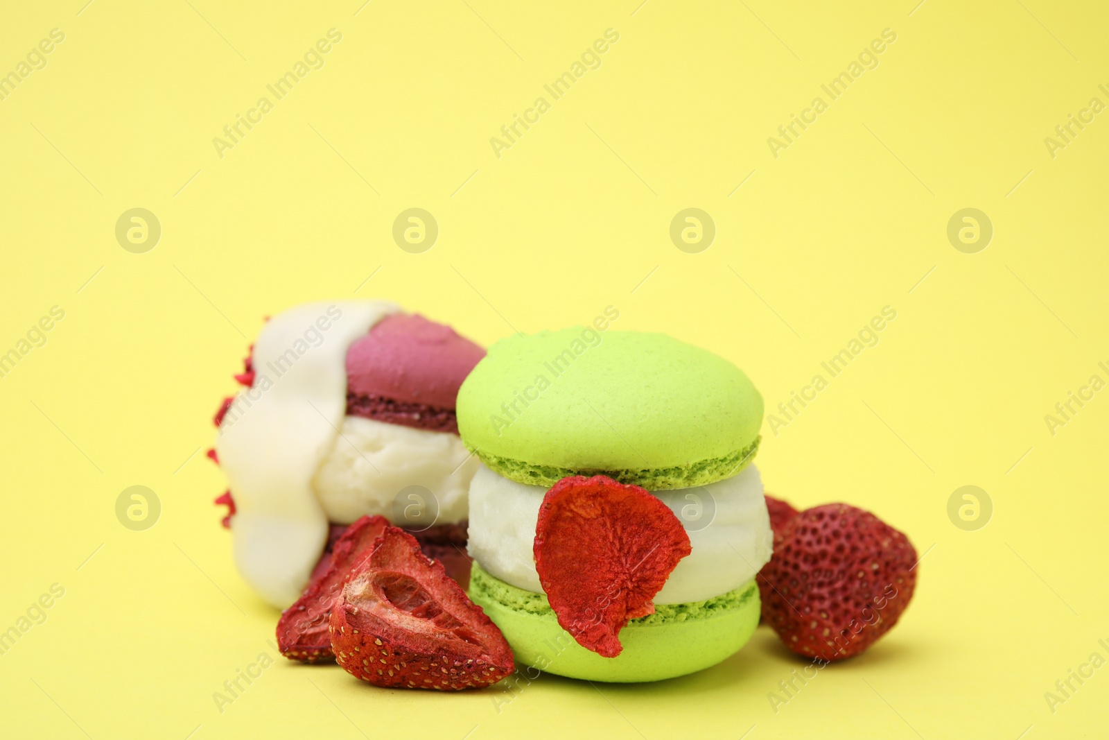 Photo of Delicious macarons and dry strawberries on yellow background, closeup
