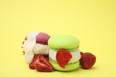 Delicious macarons and dry strawberries on yellow background, closeup