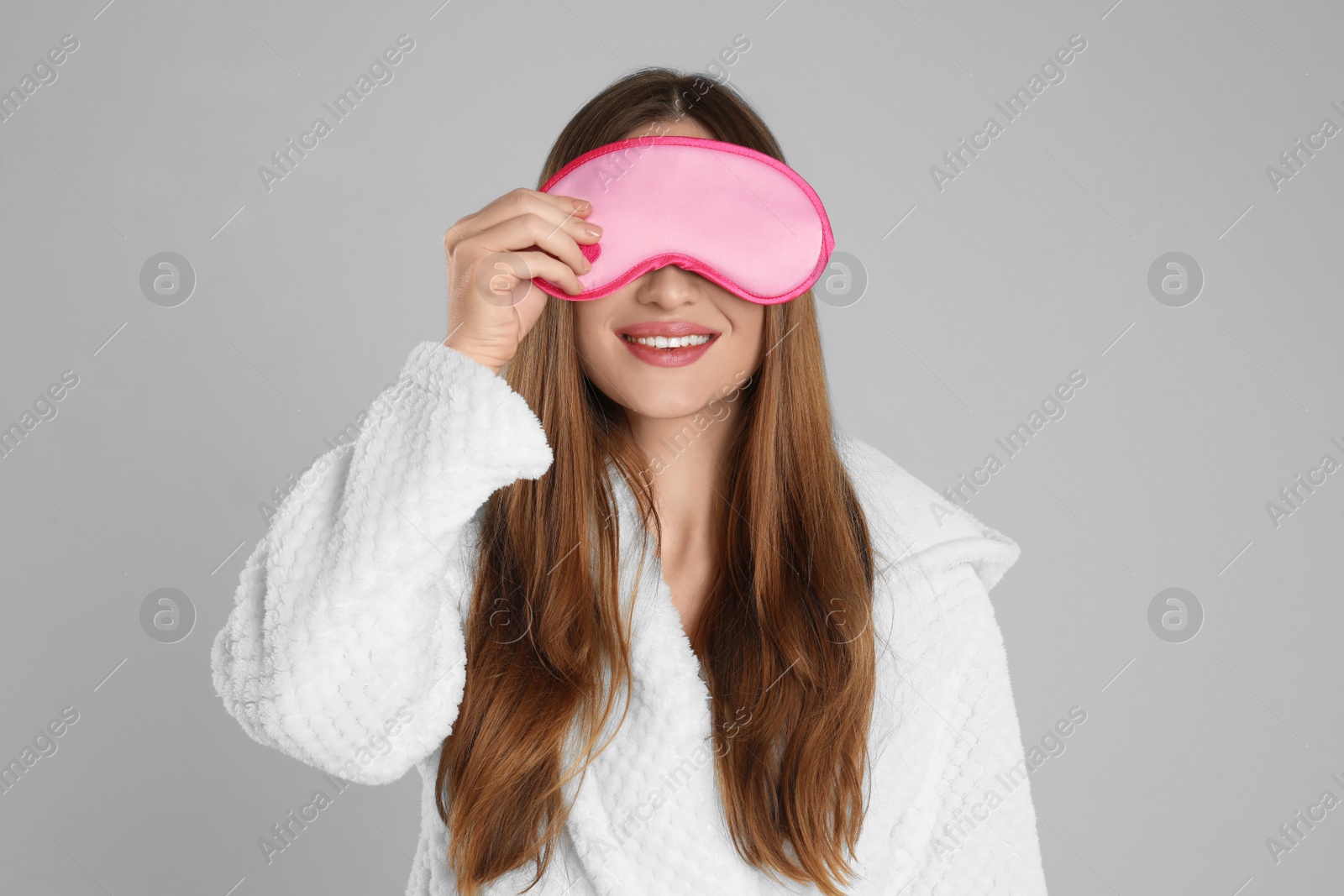 Photo of Young woman in bathrobe and eye sleeping mask on light grey background