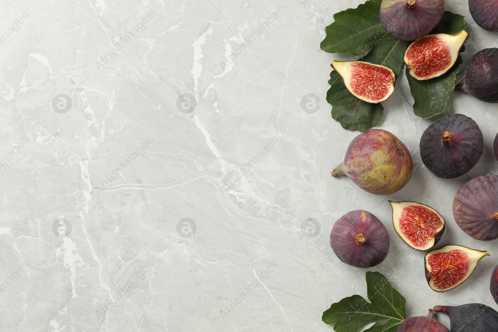 Photo of Tasty raw figs and green leaves on light grey marble table, flat lay. Space for text