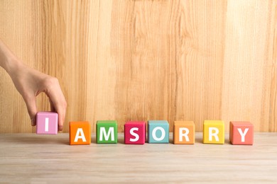 Image of Woman adding cube with letter I to make phrase I Am Sorry at wooden table, closeup. Space for text