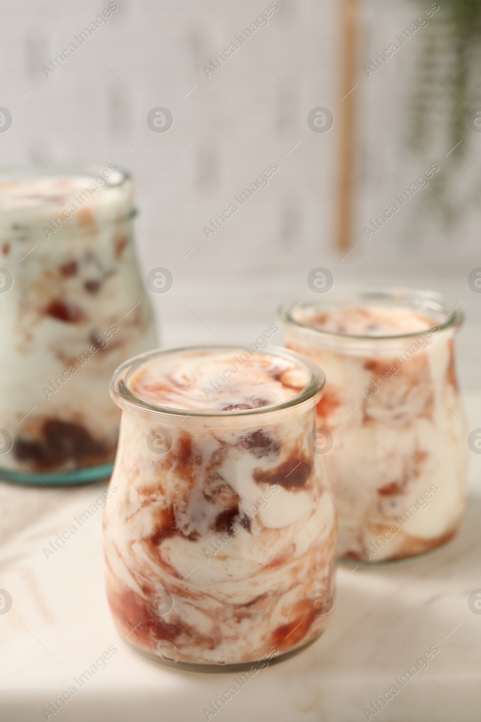 Photo of Tasty yoghurt with jam on white marble board, closeup