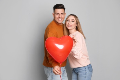 Photo of Lovely couple with heart shaped balloon on grey background. Valentine's day celebration