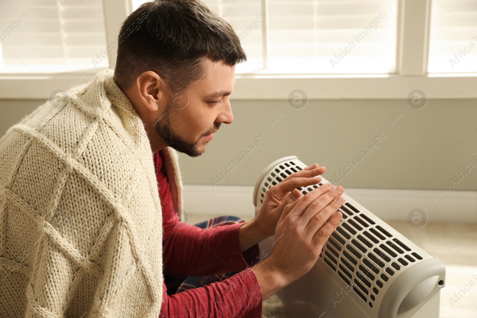 Photo of Man warming hands near electric heater at home