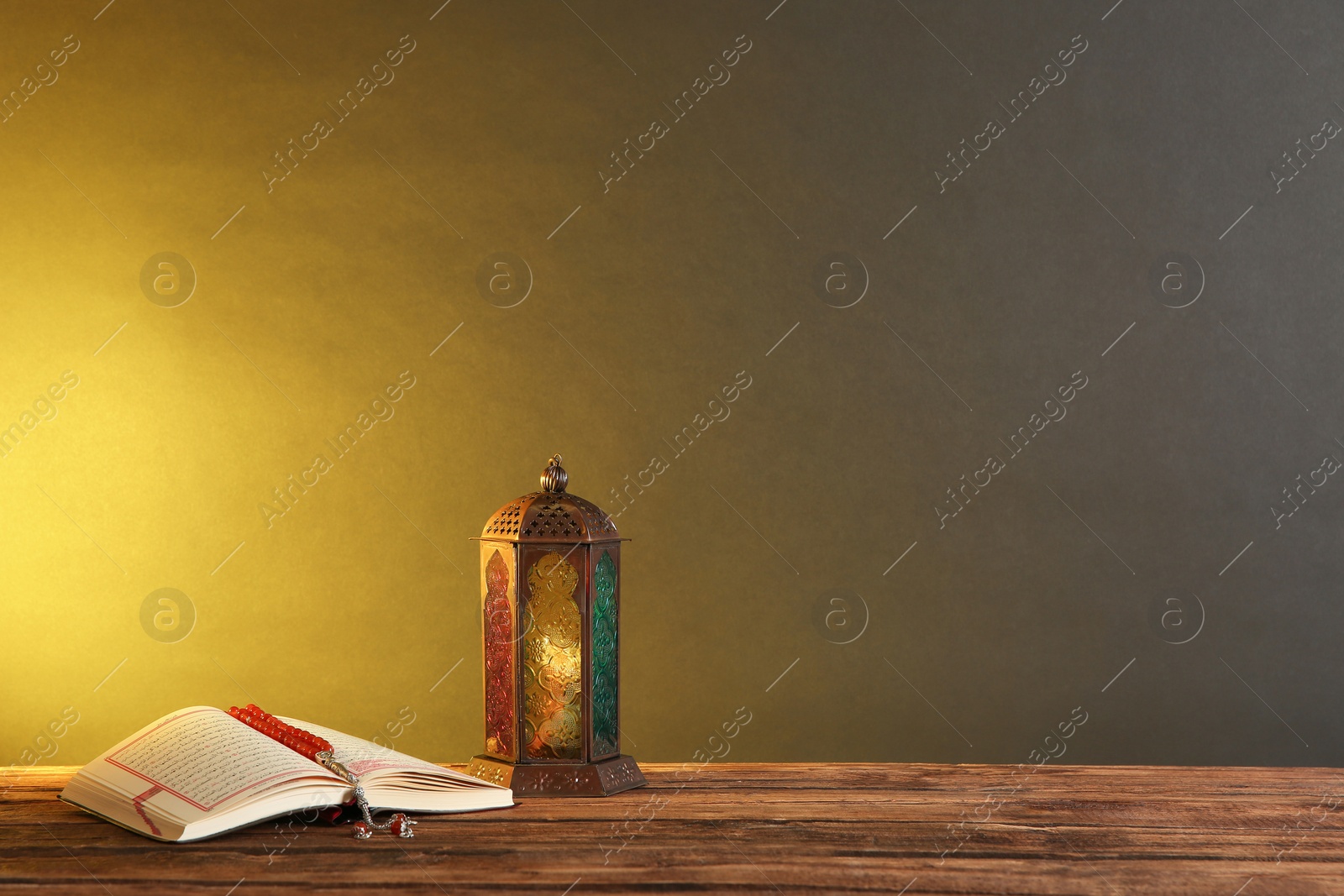 Photo of Muslim lamp, prayer beads and Koran on wooden table against dark background. Space for text