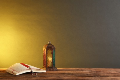 Photo of Muslim lamp, prayer beads and Koran on wooden table against dark background. Space for text