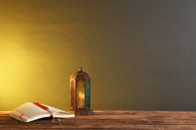 Muslim lamp, prayer beads and Koran on wooden table against dark background. Space for text