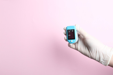 Doctor in gloves holding fingertip pulse oximeter on pink background, closeup. Space for text