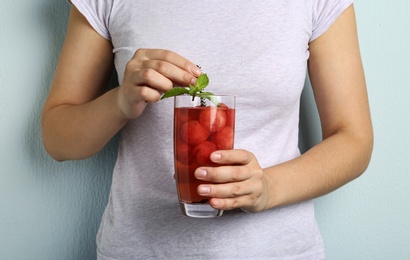 Photo of Woman holding glass of watermelon ball cocktail with mint against light blue background, closeup