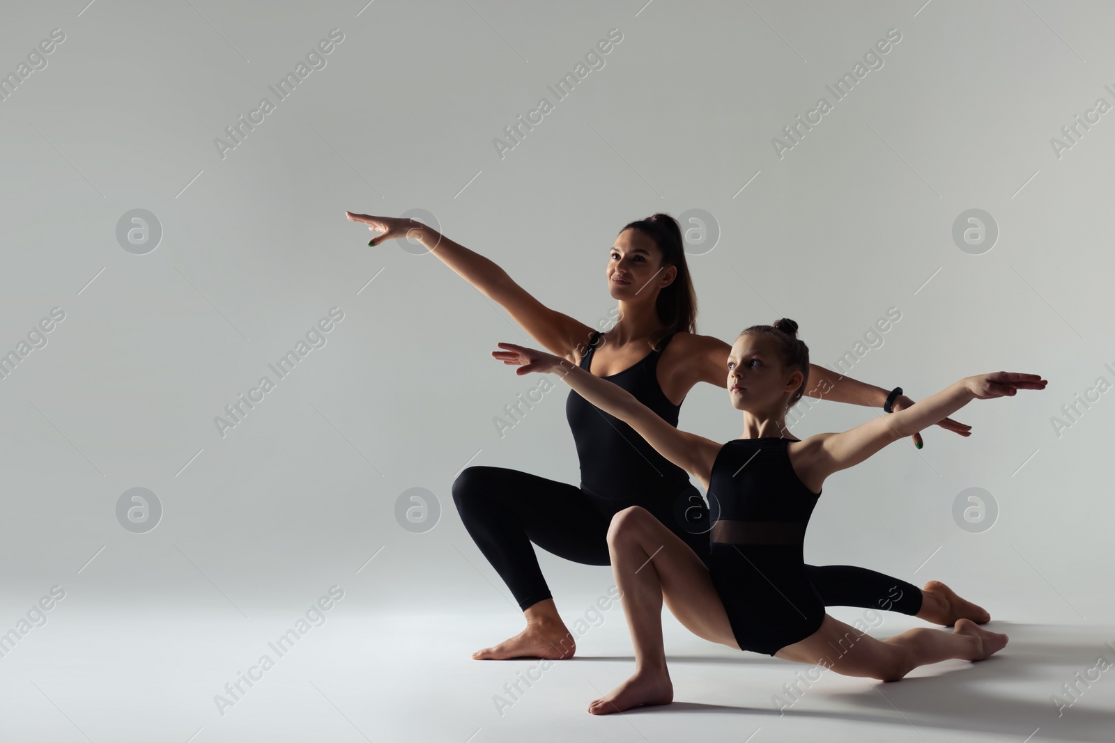 Photo of Little girl and her coach doing gymnastic exercise on white background