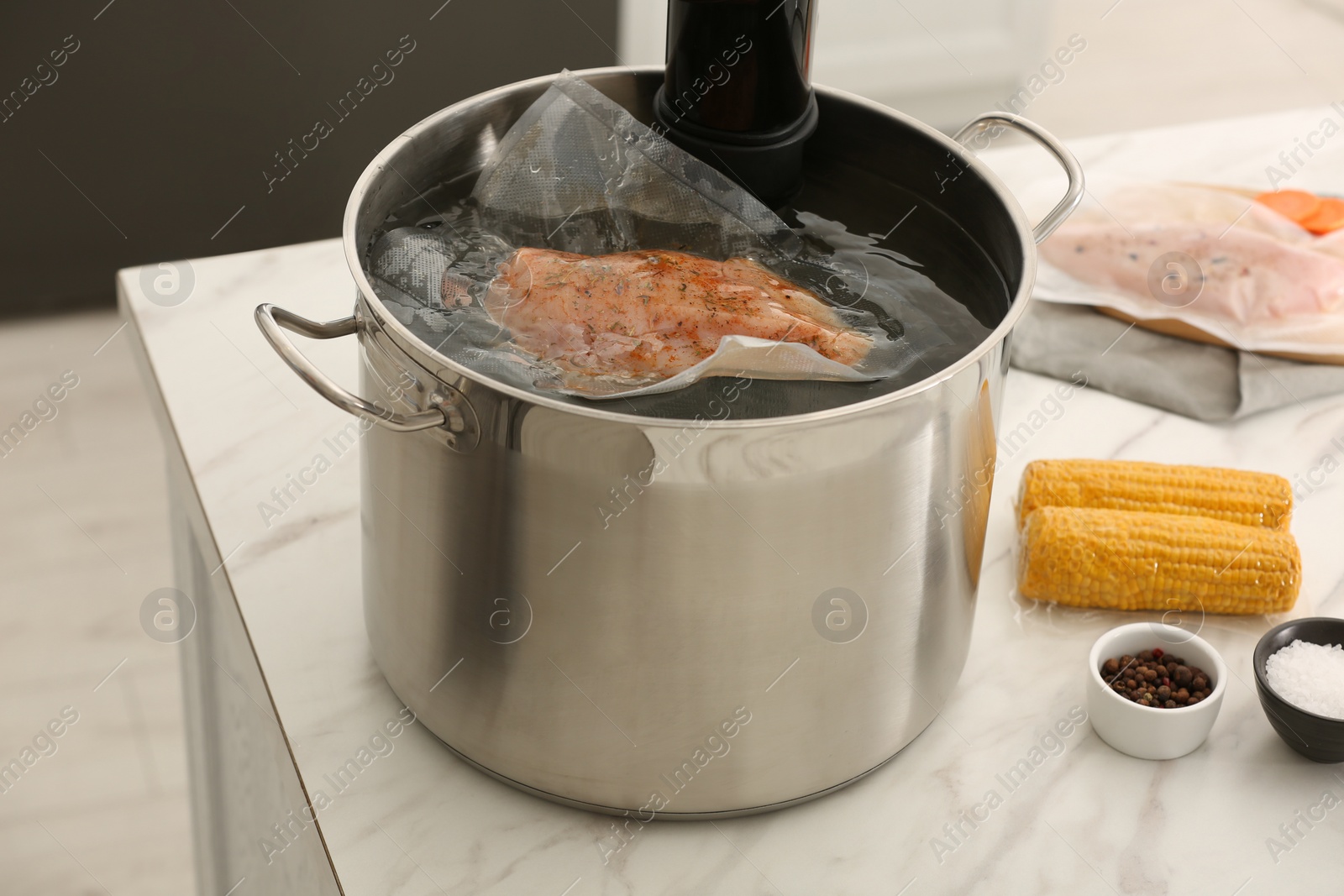 Photo of Sous vide cooker and vacuum packed meat in pot on white marble table. Thermal immersion circulator
