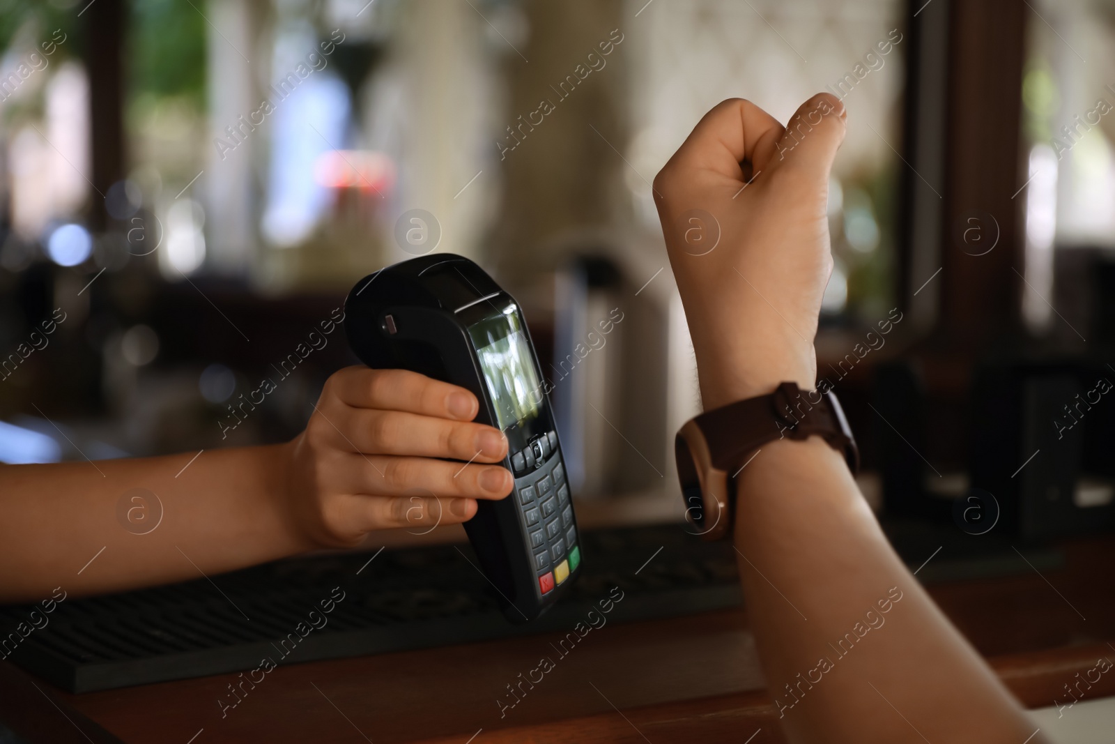 Photo of Man using terminal for contactless payment with smart watch in cafe, closeup