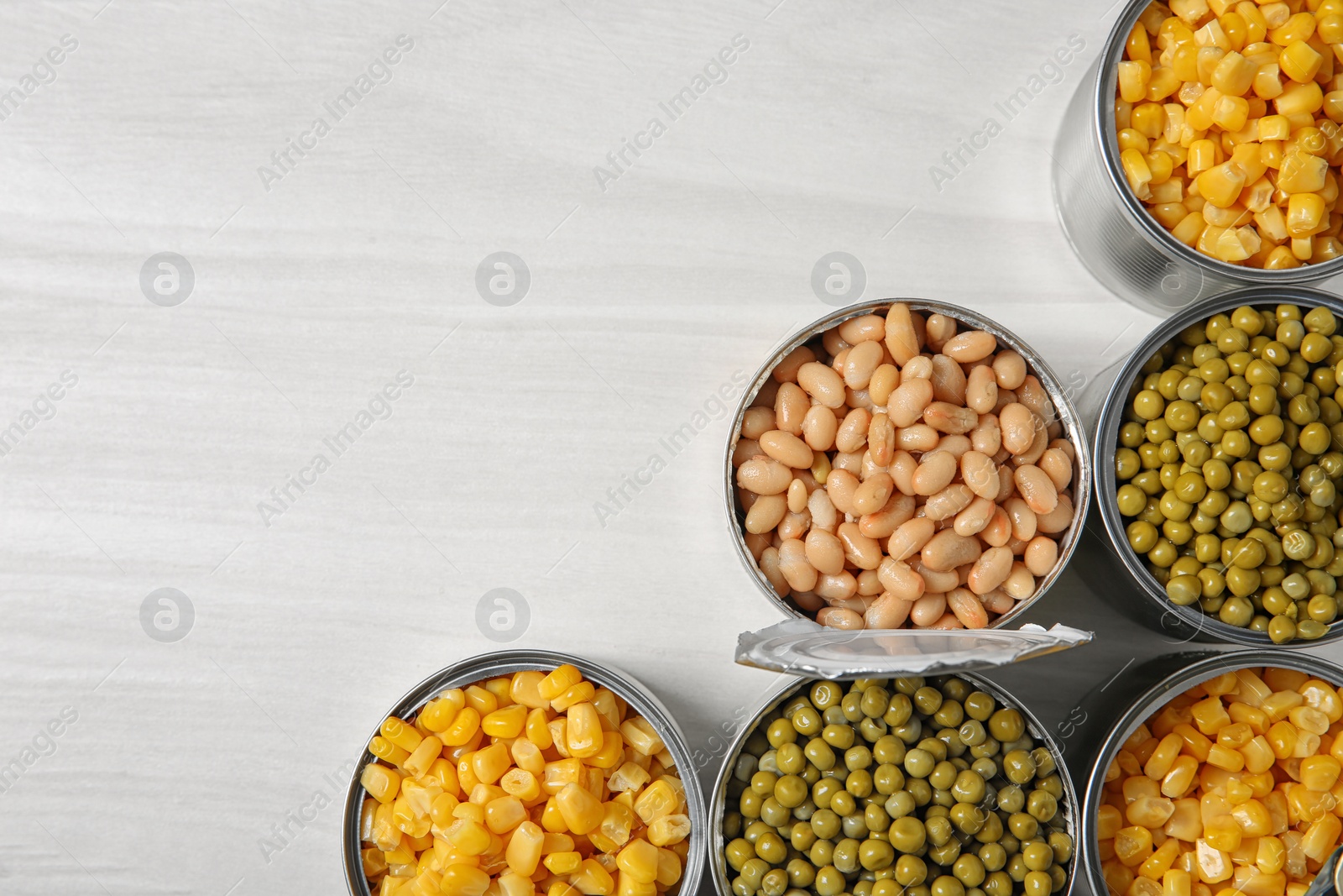 Photo of Open tin cans with different vegetables on light table, flat lay. Space for text