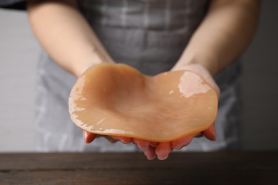 Photo of Making kombucha. Woman holding Scoby fungus at wooden table, closeup