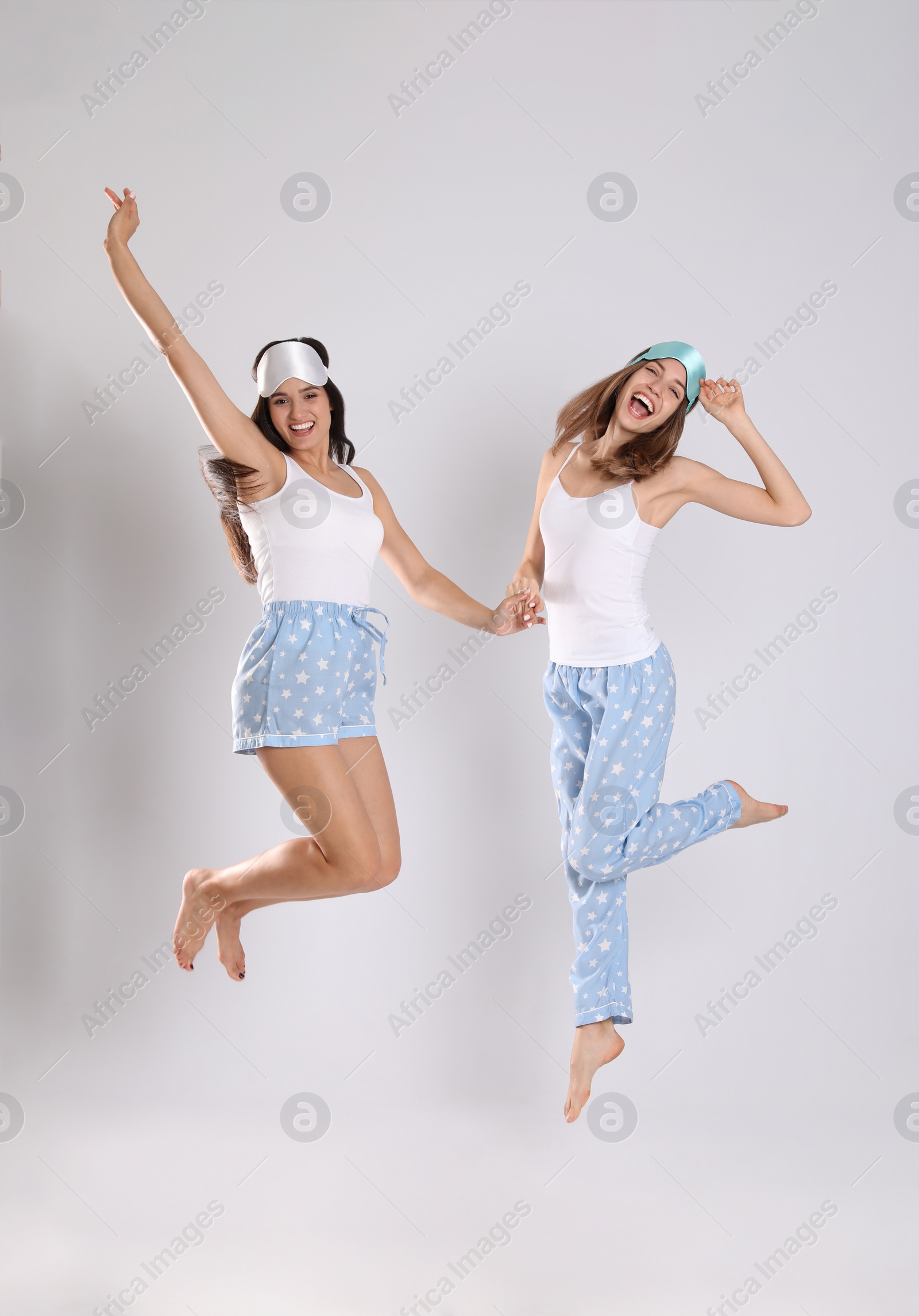 Photo of Beautiful women with sleeping masks jumping on light grey background. Bedtime