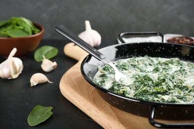 Photo of Tasty spinach dip in frying pan on black table