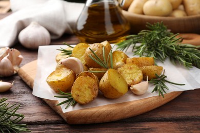 Photo of Delicious baked potatoes with rosemary and garlic on wooden table, closeup