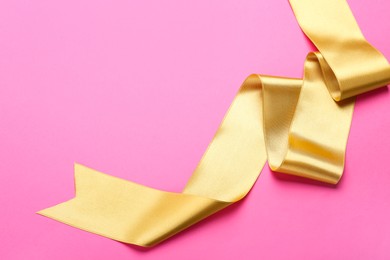 Photo of Beautiful golden ribbon on pink background, top view. Space for text