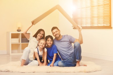 Happy family sitting under cardboard roof at home. Insurance concept