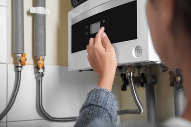 Photo of Woman pushing buttons of gas boiler indoors, closeup