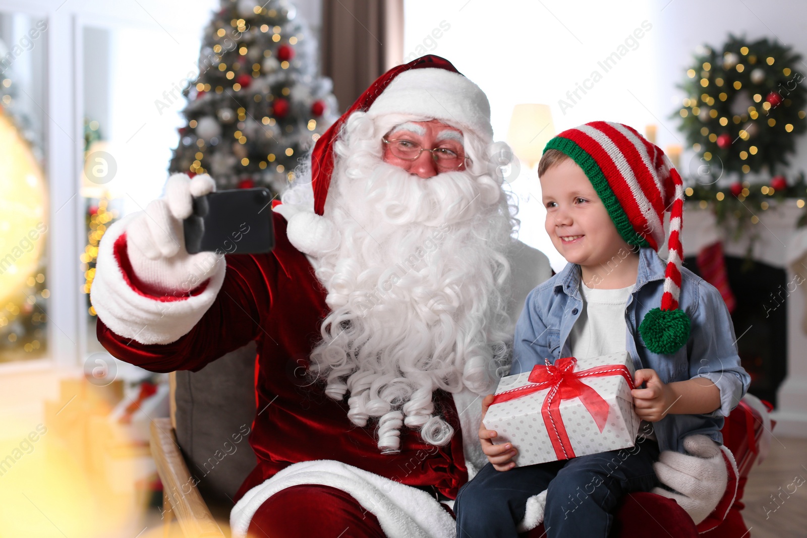 Photo of Santa Claus and little boy taking selfie in room decorated for Christmas