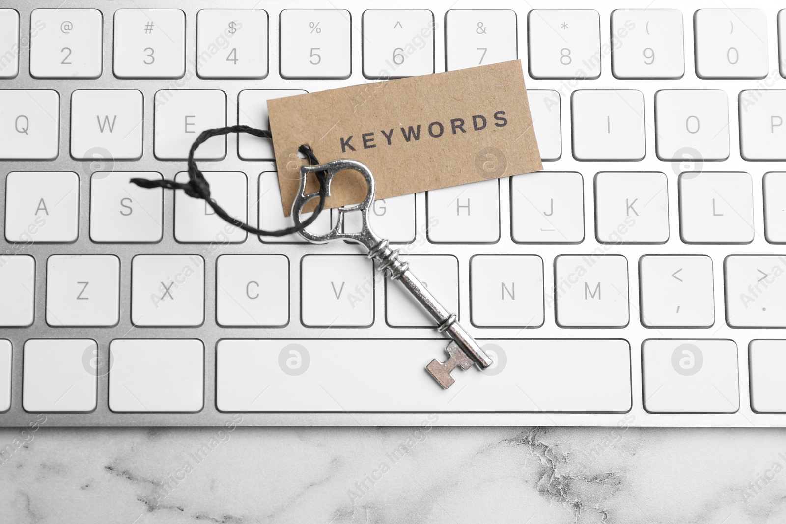 Photo of Keyboard, vintage key and tag with word KEYWORDS on white marble table, top view