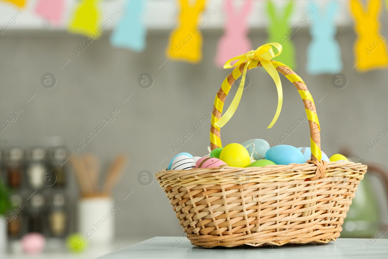 Photo of Easter basket with tasty painted eggs on white table indoors. Space for text