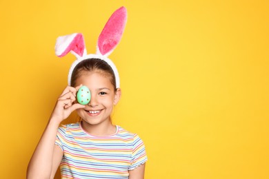 Photo of Cute happy girl with bunny ears and Easter egg against yellow background. Space for text