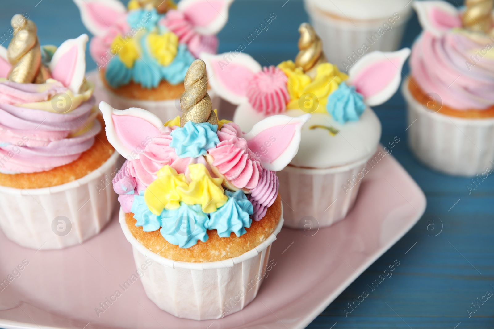 Photo of Plate with cute sweet unicorn cupcakes on light blue wooden table, closeup