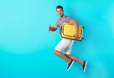 Photo of Young man jumping with suitcase on color background. Space for text