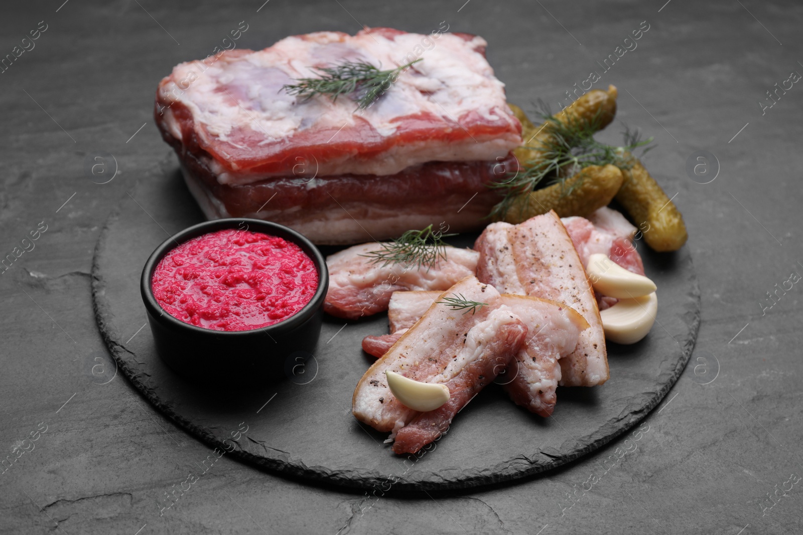 Photo of Tasty pork fatback with spices, pickled cucumbers and sauce on black table