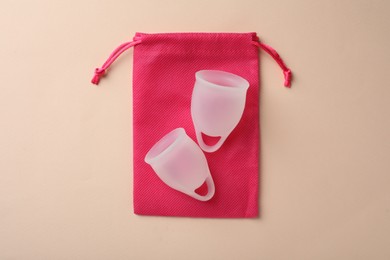 Photo of Menstrual cups with cotton bag on beige background, top view
