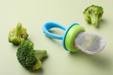 Photo of Nibbler with boiled broccoli on green background. Baby feeder