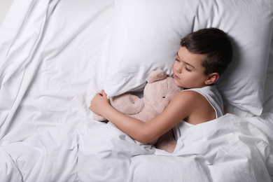 Little boy sleeping with teddy bear at home, top view. Bedtime