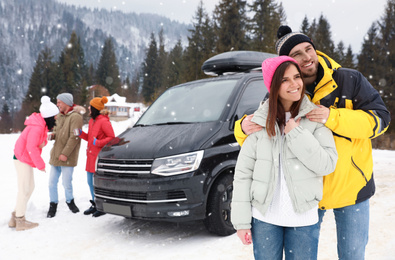 Happy couple and their friends near car on snowy road. Winter vacation