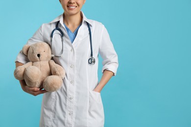Photo of Pediatrician with teddy bear and stethoscope on turquoise background, closeup. Space for text